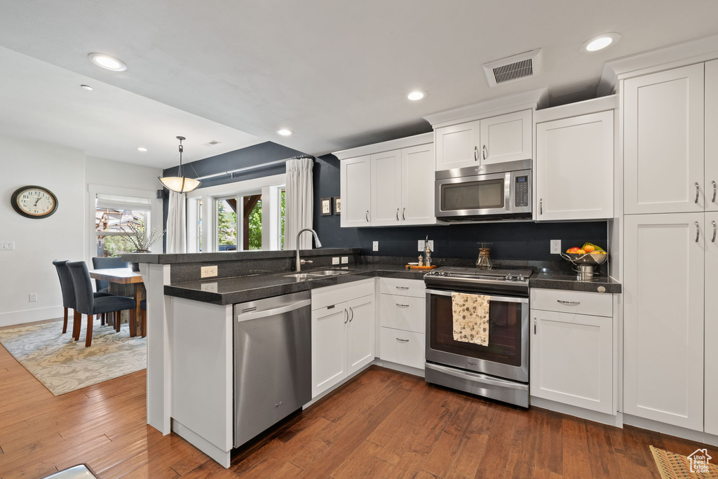 Kitchen featuring appliances with stainless steel finishes, a peninsula, a sink, white cabinets, and dark wood-style floors