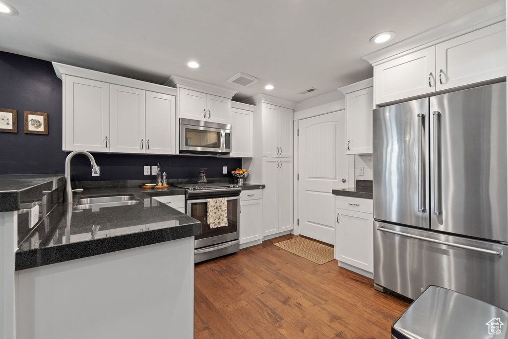 Kitchen featuring appliances with stainless steel finishes, a sink, recessed lighting, white cabinets, and dark countertops