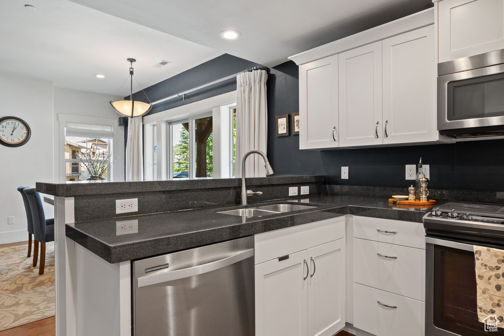 Kitchen featuring stainless steel appliances, a sink, a peninsula, white cabinets, and wood finished floors