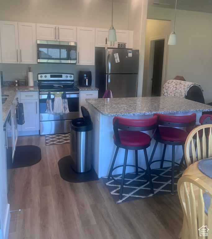 Kitchen with appliances with stainless steel finishes, dark wood finished floors, white cabinets, a breakfast bar, and pendant lighting