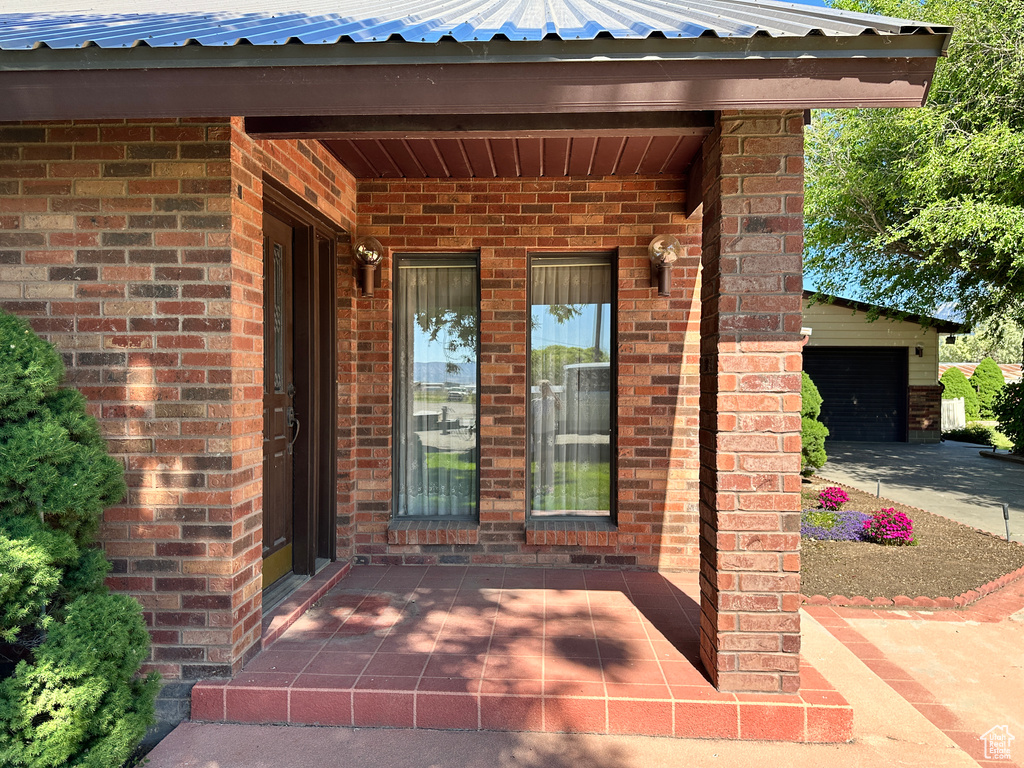 Doorway to property featuring brick siding, a garage, and metal roof