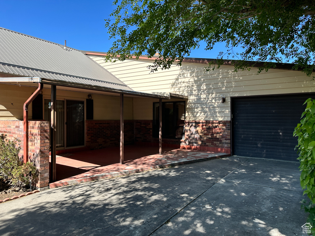 Exterior space featuring brick siding, driveway, a garage, and metal roof