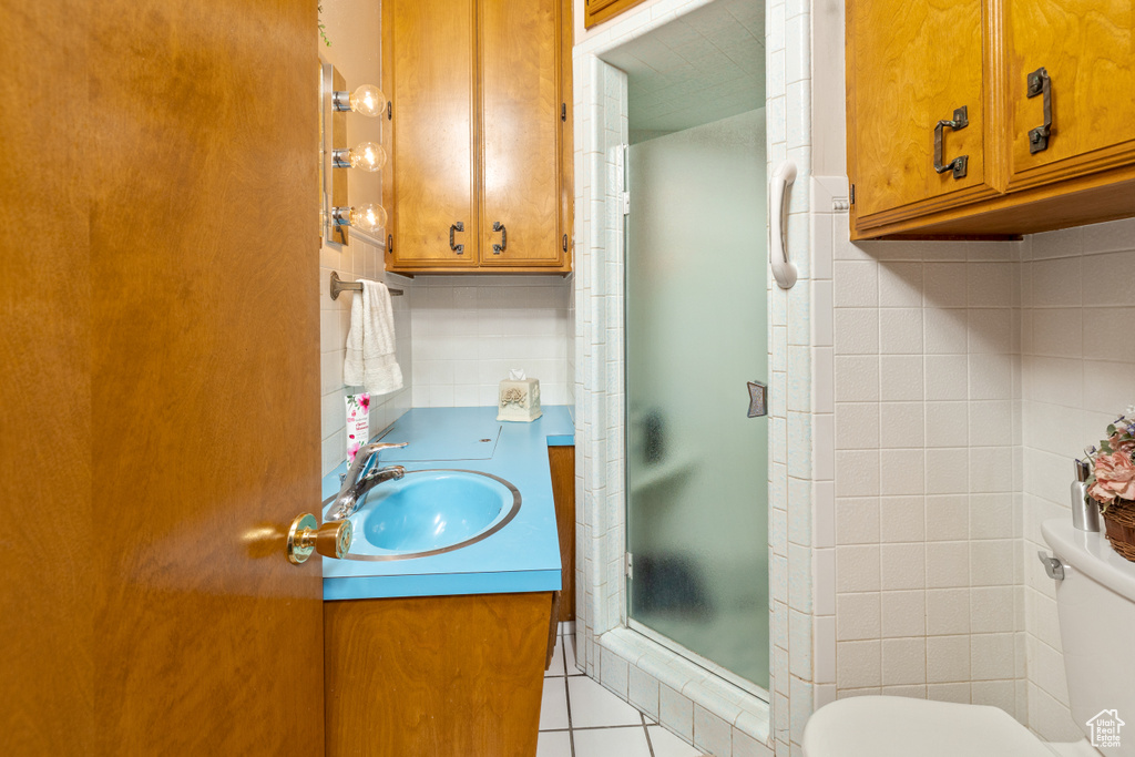 Full bathroom with toilet, a stall shower, vanity, tile walls, and tile patterned flooring