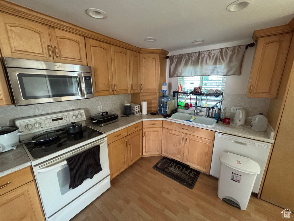 Kitchen featuring white appliances, a sink, light countertops, decorative backsplash, and light wood-style floors