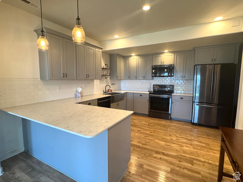 Kitchen with stainless steel appliances, gray cabinetry, a peninsula, tasteful backsplash, and light stone counters