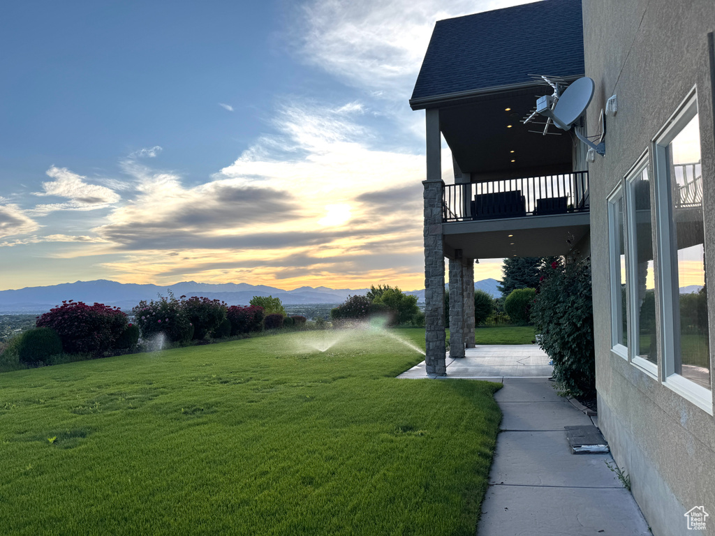 View of grassy yard featuring a balcony and a mountain view