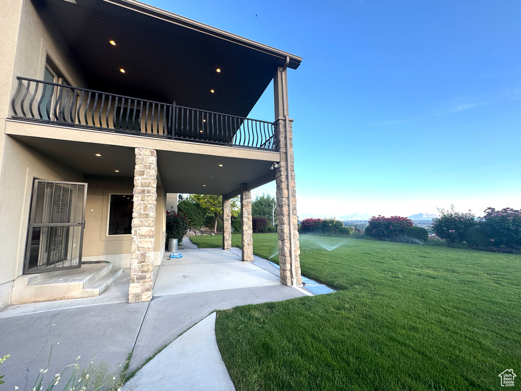 View of grassy yard featuring a patio and a balcony