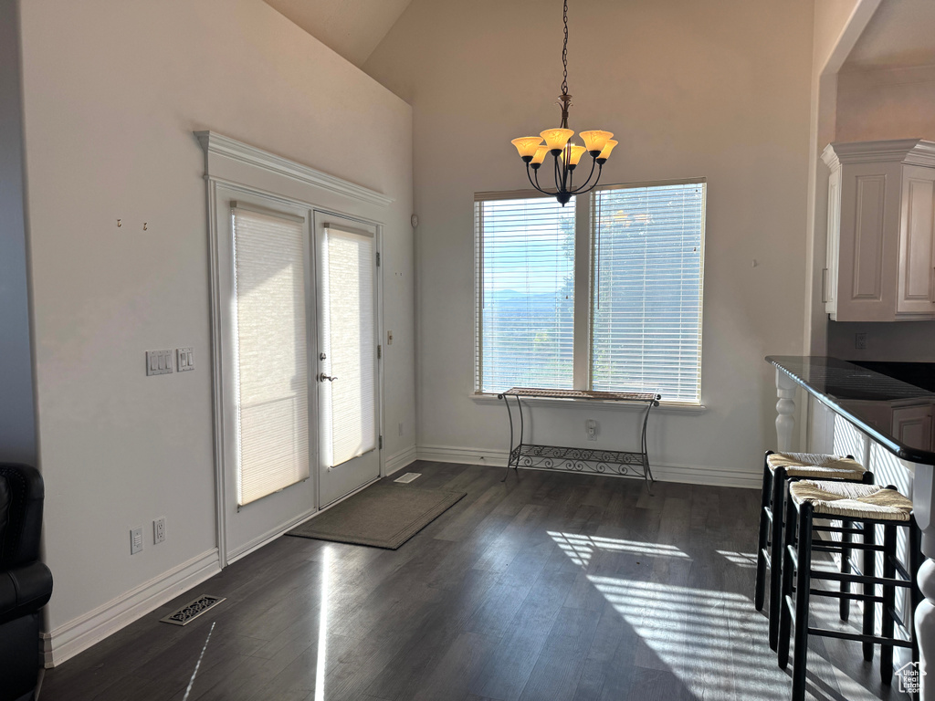 Unfurnished dining area featuring french doors, dark wood finished floors, a chandelier, baseboards, and high vaulted ceiling