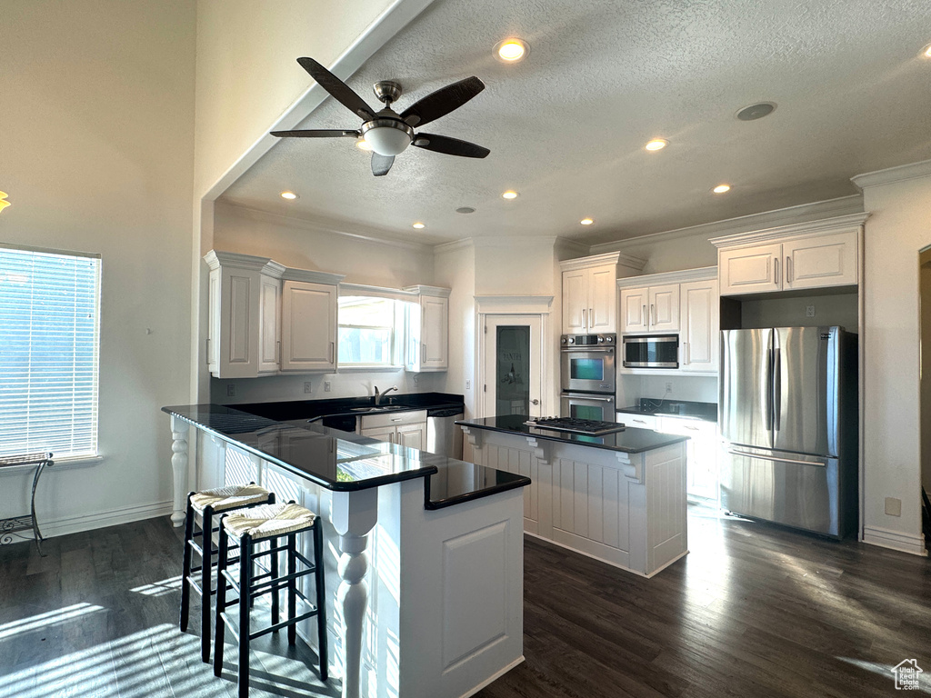 Kitchen with appliances with stainless steel finishes, a sink, dark countertops, a center island, and a textured ceiling