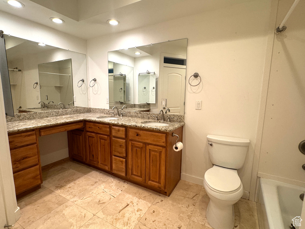 Bathroom featuring baseboards, a tub, double vanity, recessed lighting, and toilet