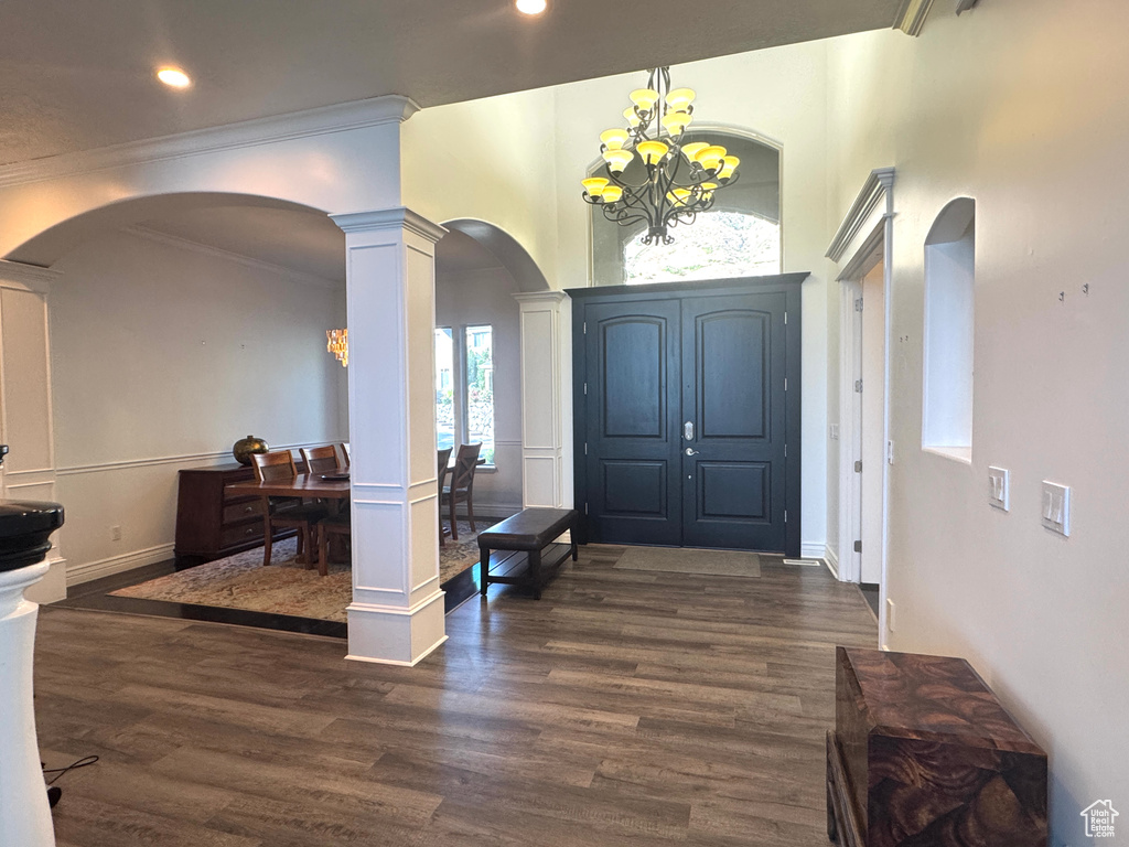 Entrance foyer featuring arched walkways, ornate columns, a chandelier, dark wood-type flooring, and crown molding