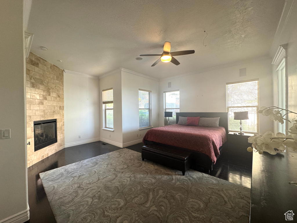 Bedroom featuring dark wood-type flooring, a fireplace, ceiling fan, crown molding, and a textured ceiling