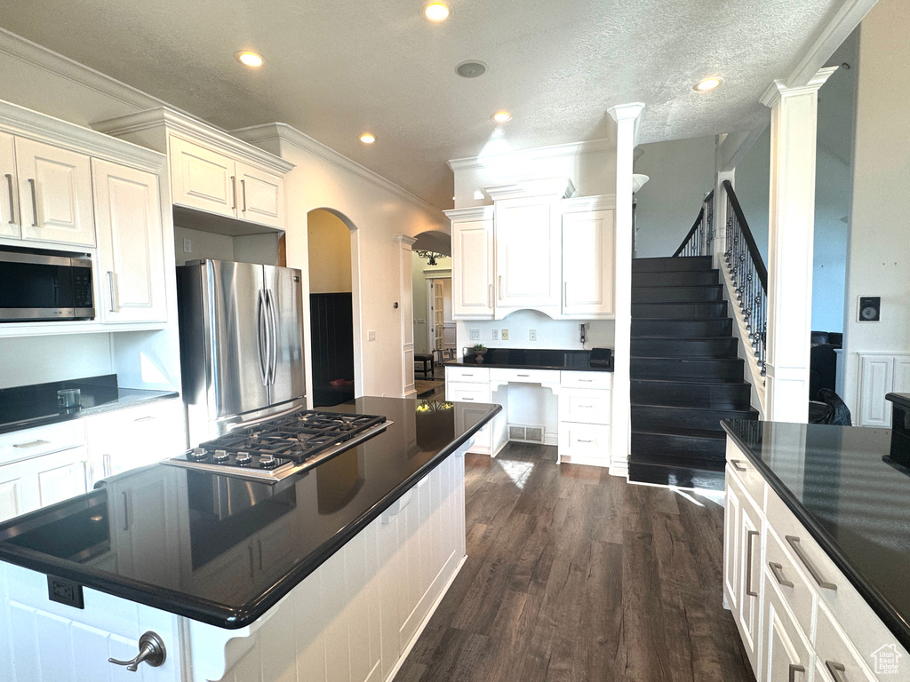 Kitchen with appliances with stainless steel finishes, dark countertops, dark wood-style flooring, ornamental molding, and arched walkways