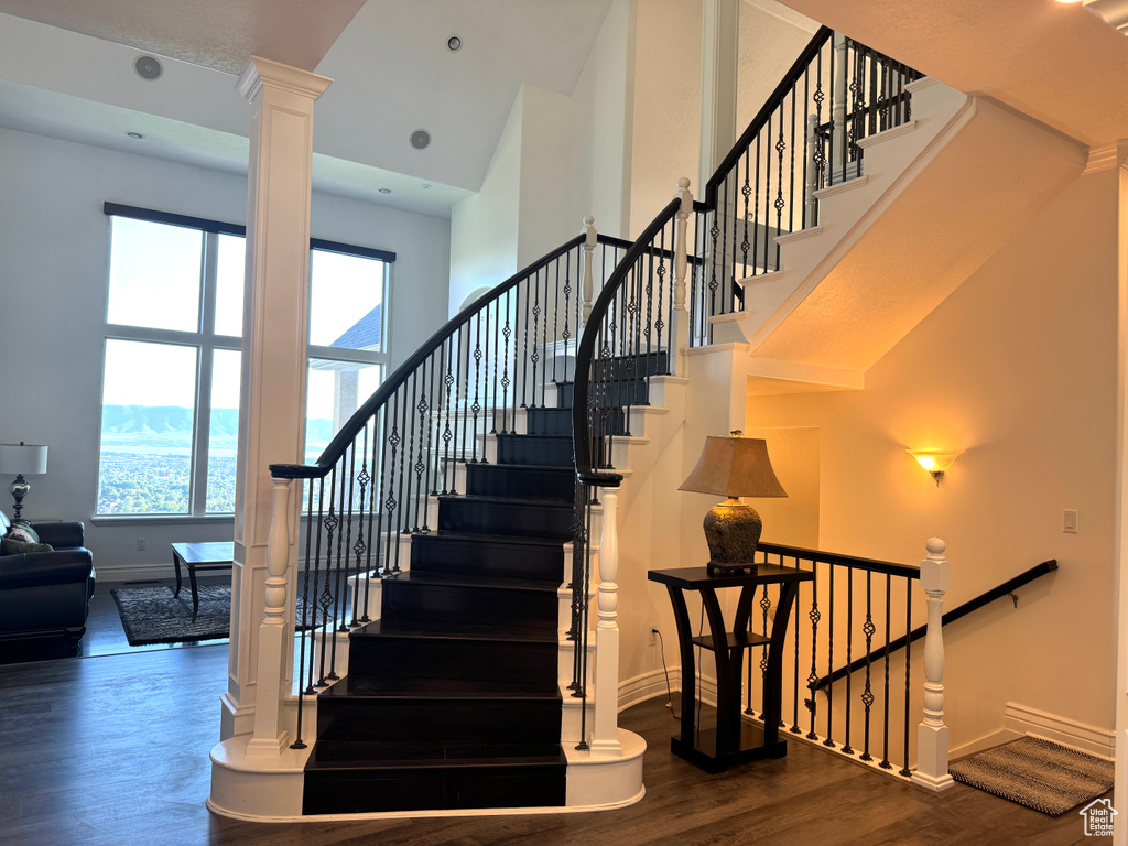 Staircase with a towering ceiling, plenty of natural light, wood finished floors, baseboards, and ornate columns