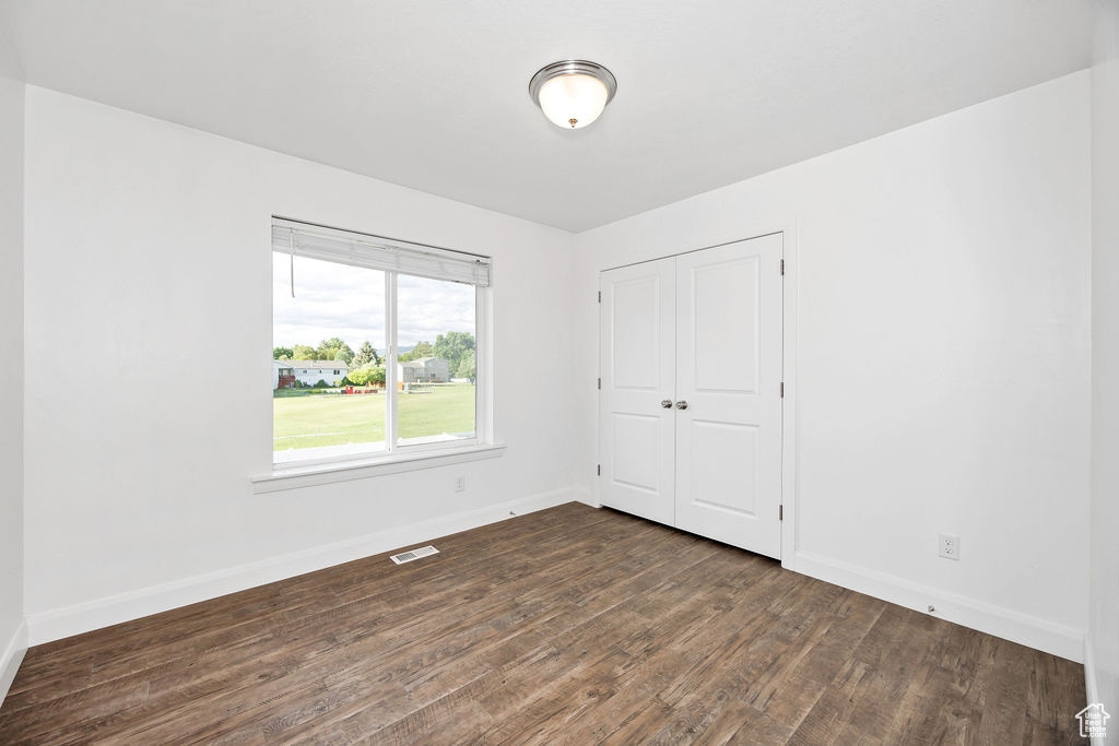 Unfurnished bedroom with dark wood finished floors, baseboards, and a closet