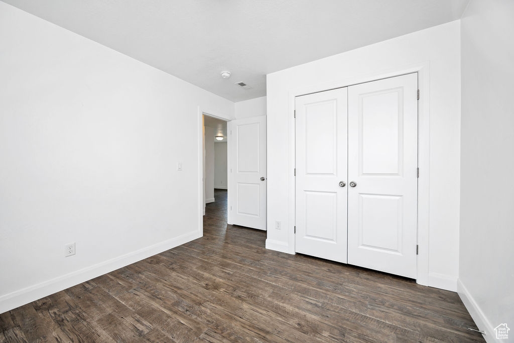 Unfurnished bedroom featuring baseboards, dark wood-style floors, and a closet