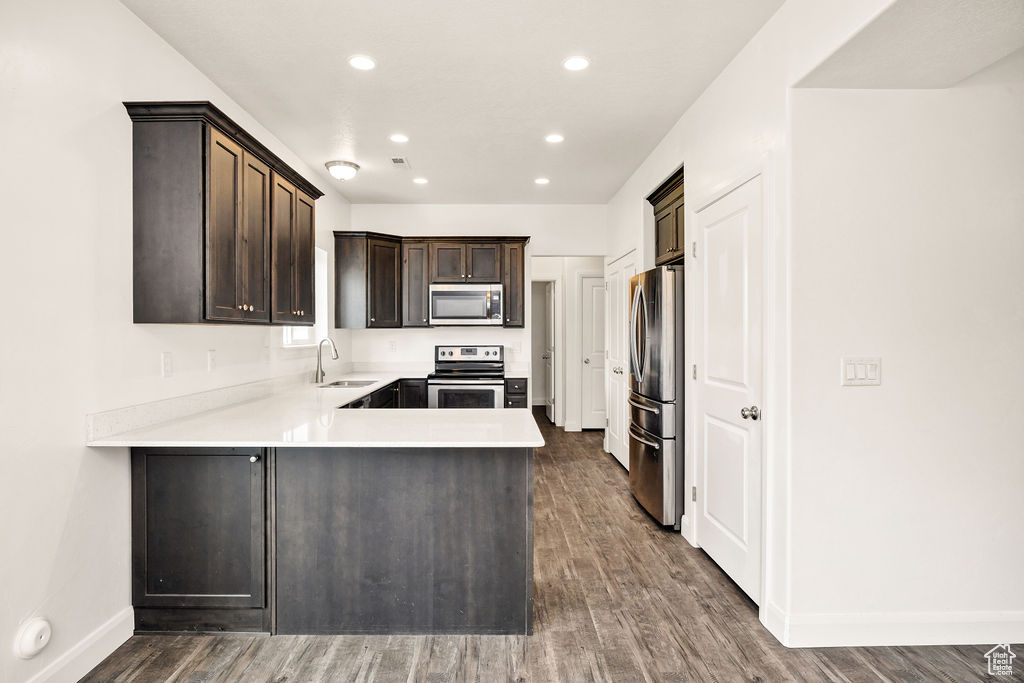 Kitchen featuring appliances with stainless steel finishes, a sink, dark brown cabinetry, a peninsula, and wood finished floors