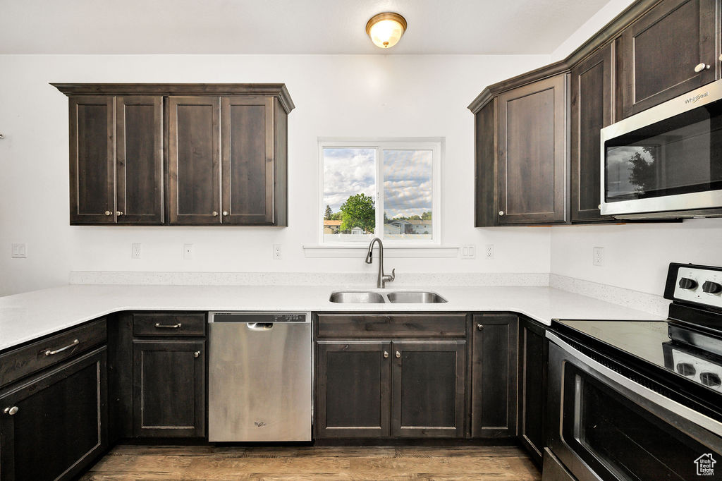 Kitchen featuring appliances with stainless steel finishes, a sink, light wood finished floors, and dark brown cabinets