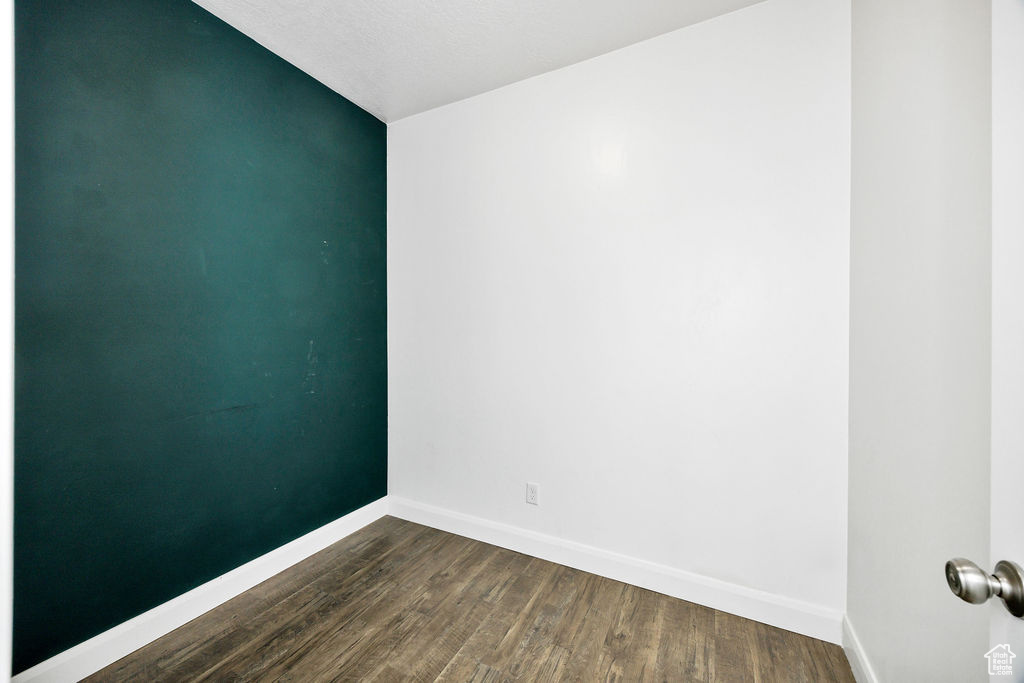 Spare room featuring dark wood-style flooring, baseboards, and lofted ceiling