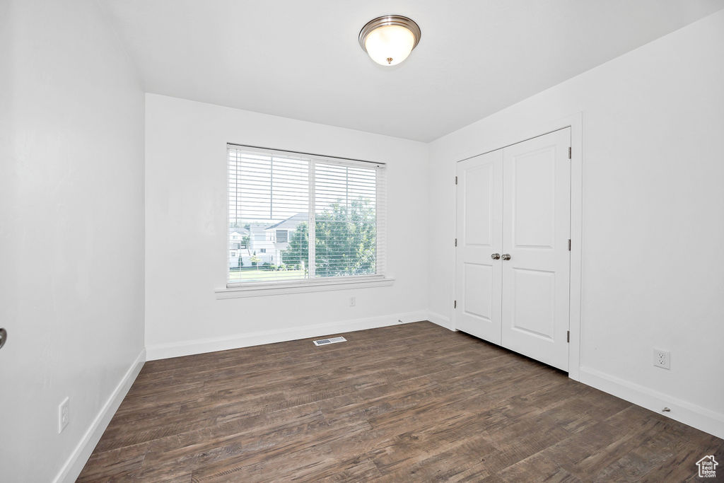 Unfurnished bedroom featuring dark wood-style flooring, baseboards, and a closet