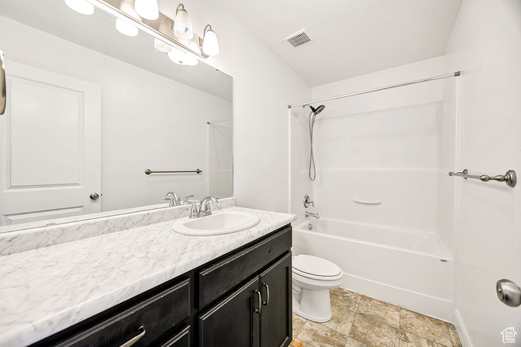 Full bath with vanity, washtub / shower combination, toilet, and stone finish flooring