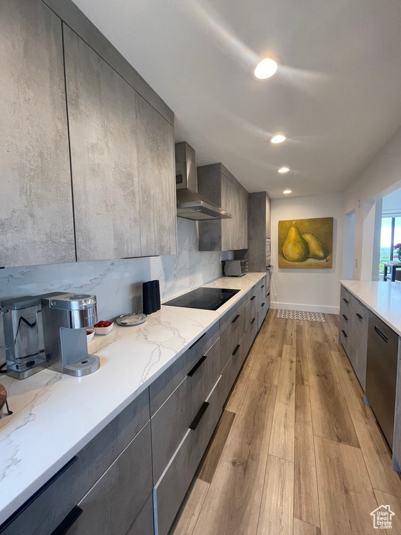 Kitchen with wall chimney exhaust hood, modern cabinets, black electric stovetop, light wood-style flooring, and stainless steel dishwasher