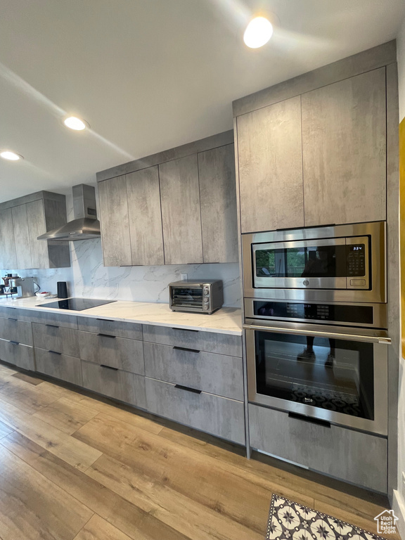 Kitchen with wall chimney exhaust hood, appliances with stainless steel finishes, gray cabinetry, and light wood finished floors