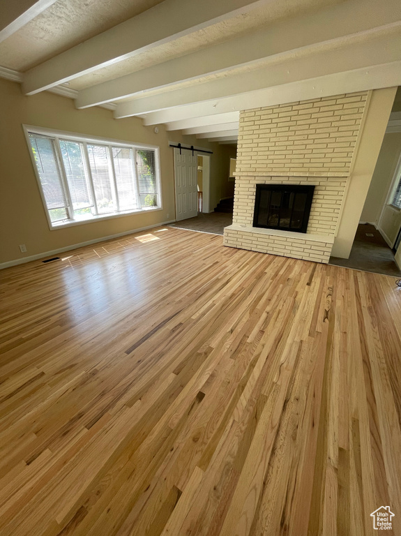 Unfurnished living room featuring a barn door, beamed ceiling, wood finished floors, a fireplace, and baseboards