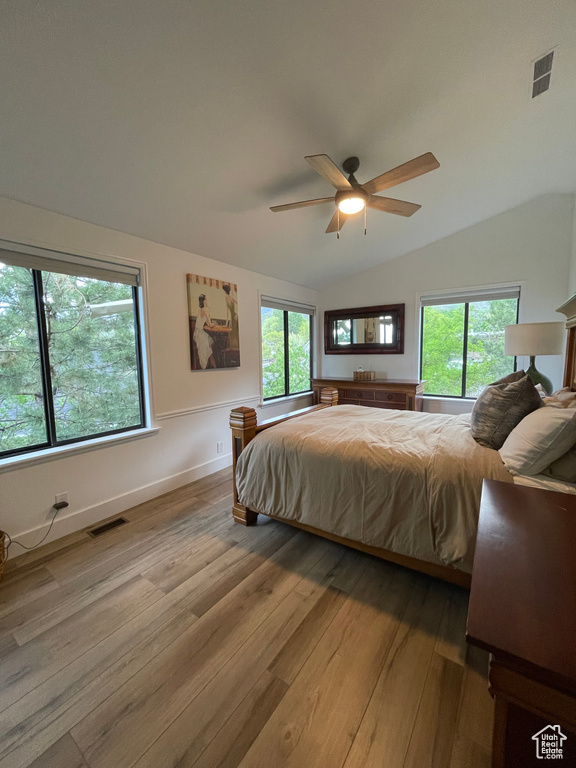 Bedroom featuring light wood finished floors, vaulted ceiling, multiple windows, baseboards, and ceiling fan