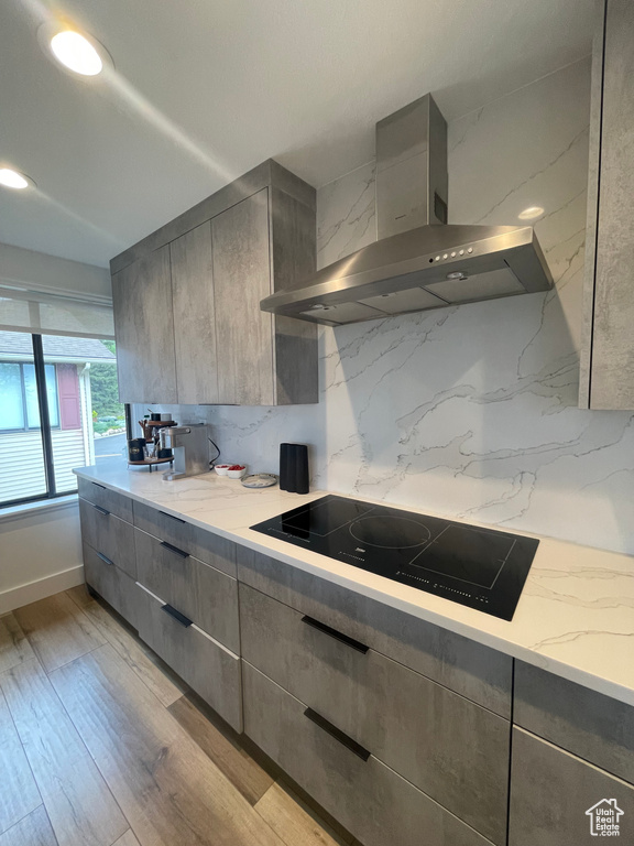 Kitchen featuring wall chimney exhaust hood, black electric stovetop, decorative backsplash, modern cabinets, and gray cabinets