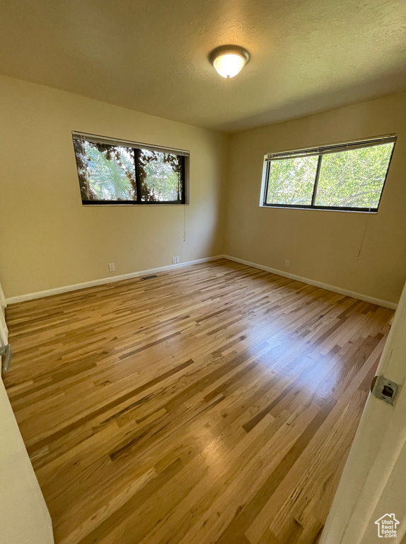 Spare room featuring light wood-style floors, baseboards, and a textured ceiling