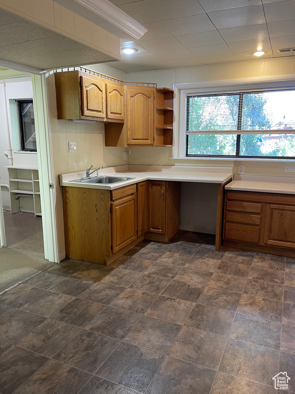 Kitchen featuring a sink, light countertops, built in desk, and brown cabinetry