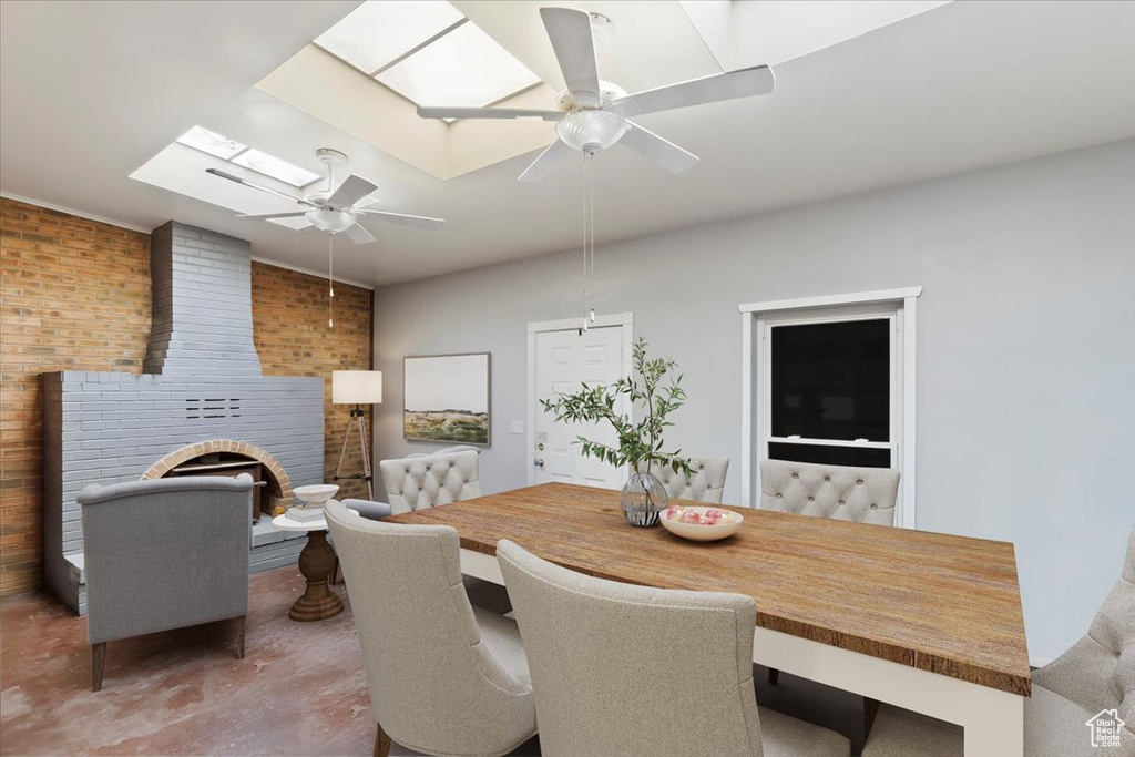 Dining room featuring a skylight, ceiling fan, and brick wall