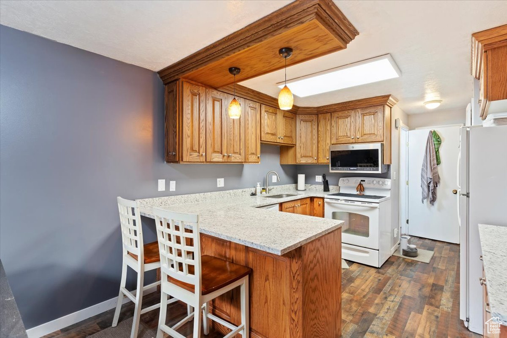 Kitchen featuring white appliances, a sink, a peninsula, light countertops, and pendant lighting
