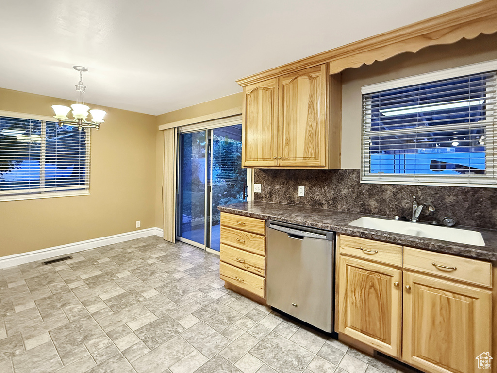 Kitchen with stainless steel dishwasher, light brown cabinets, baseboards, a sink, and a chandelier