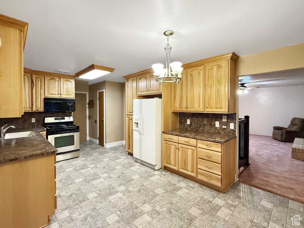 Kitchen featuring gas stove, black microwave, white refrigerator with ice dispenser, a sink, and decorative backsplash