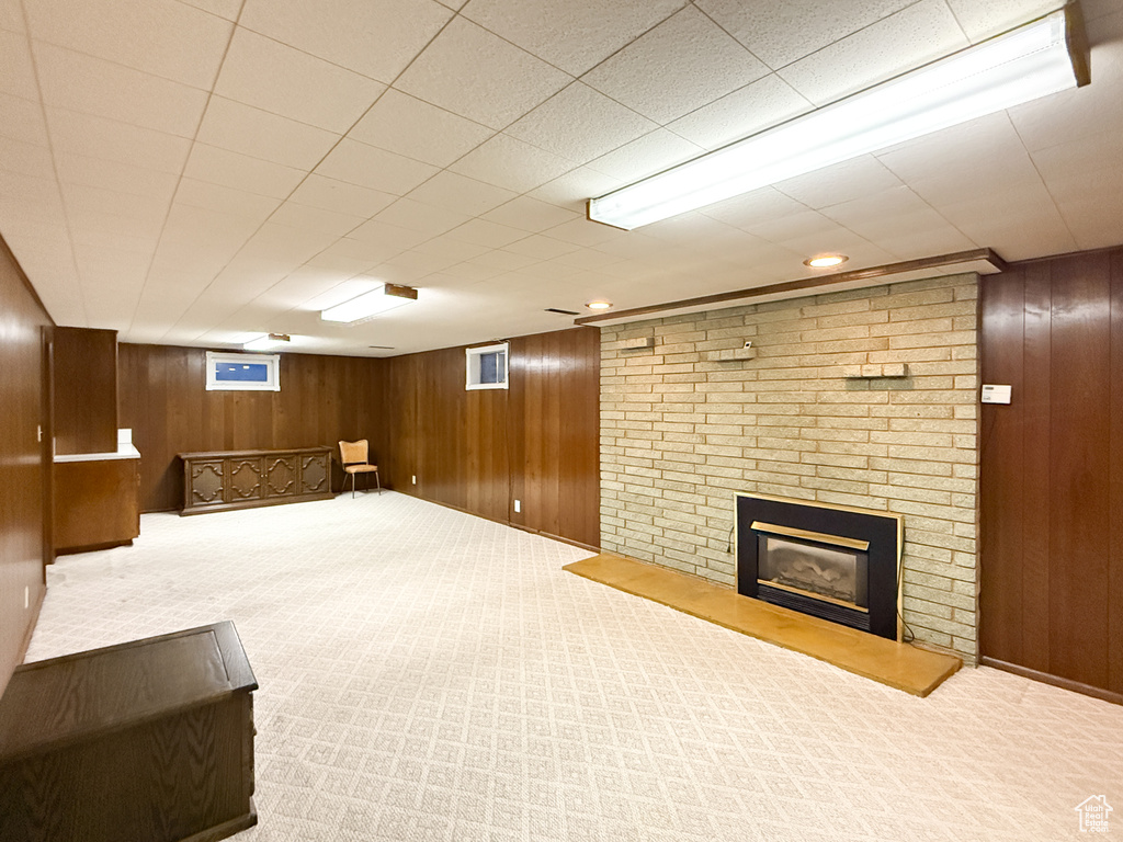 Finished basement featuring wooden walls, carpet, and a brick fireplace