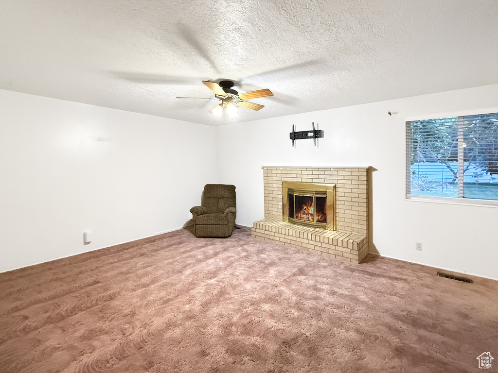 Unfurnished living room featuring ceiling fan, a brick fireplace, a textured ceiling, and carpet