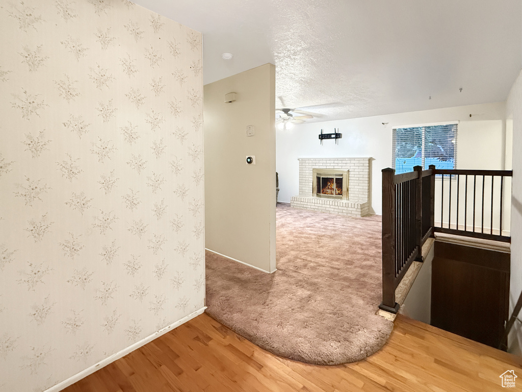 Hall with baseboards, wood finished floors, wallpapered walls, an upstairs landing, and a textured ceiling
