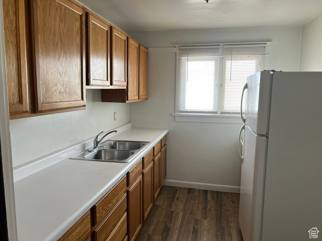 Kitchen with freestanding refrigerator, a sink, dark wood finished floors, light countertops, and brown cabinetry
