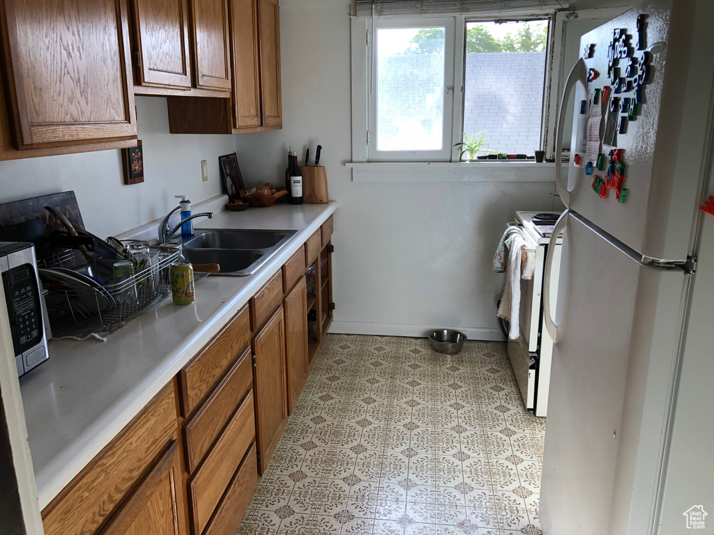 Kitchen with white appliances, a sink, brown cabinets, and light countertops