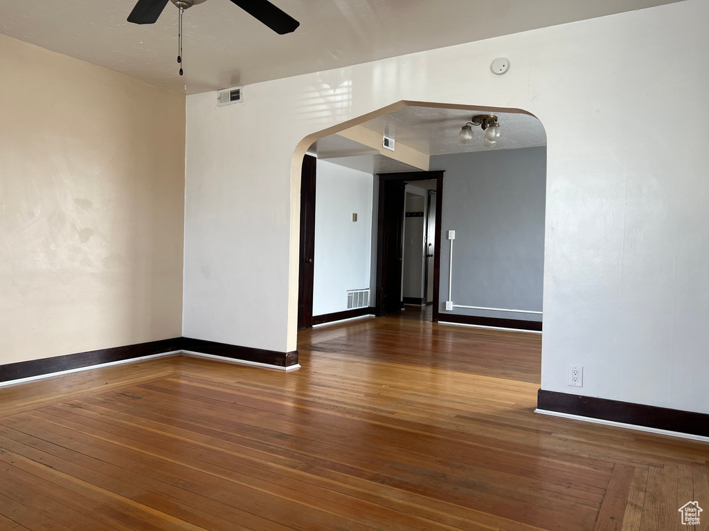Empty room featuring arched walkways, ceiling fan, wood-type flooring, baseboards, and a smoke detector