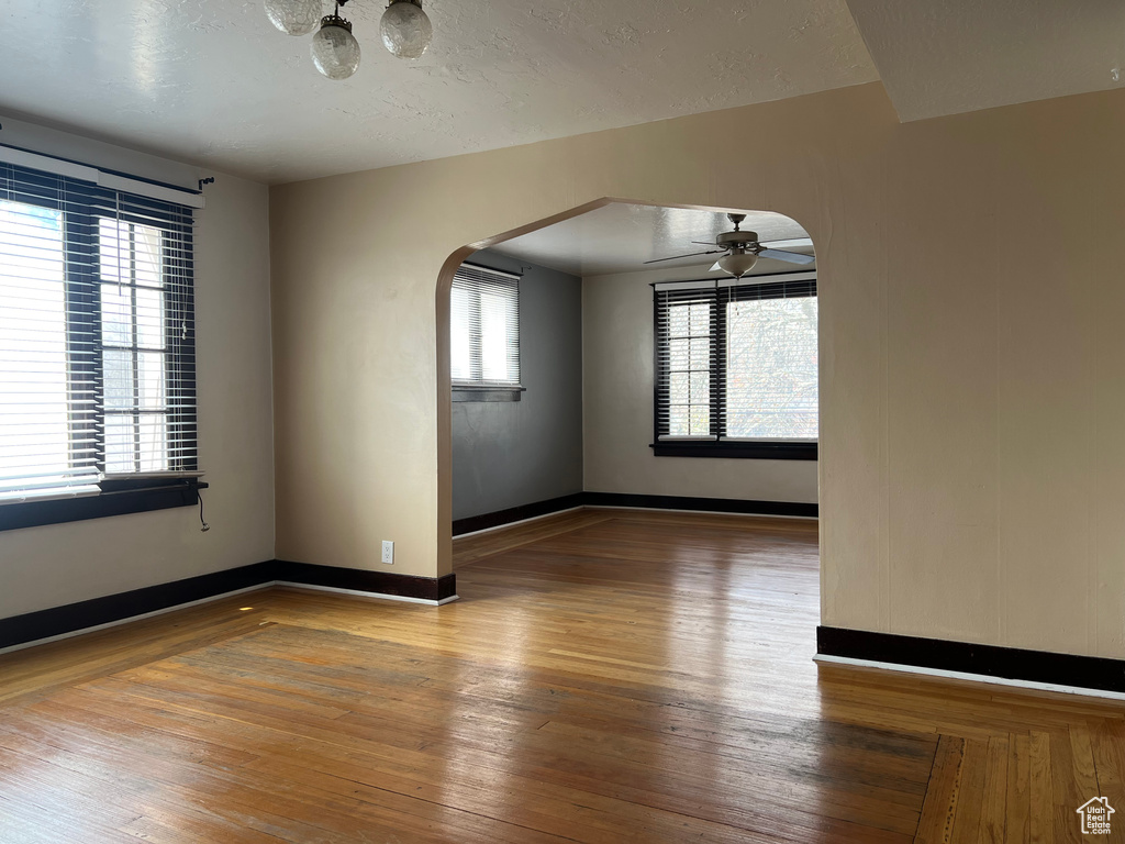 Spare room with arched walkways, wood-type flooring, ceiling fan, baseboards, and a textured ceiling