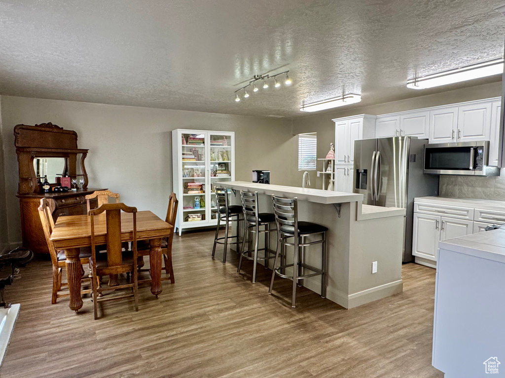 Dining room featuring a textured ceiling, light wood finished floors, baseboards, and track lighting