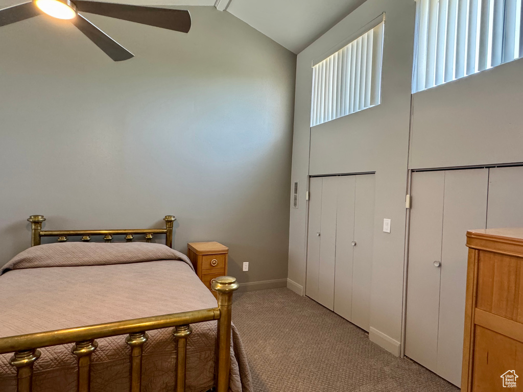 Bedroom with light carpet, ceiling fan, baseboards, and high vaulted ceiling