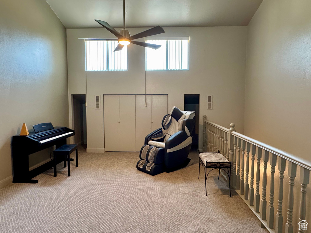 Living area with a ceiling fan, carpet flooring, a high ceiling, baseboards, and an upstairs landing