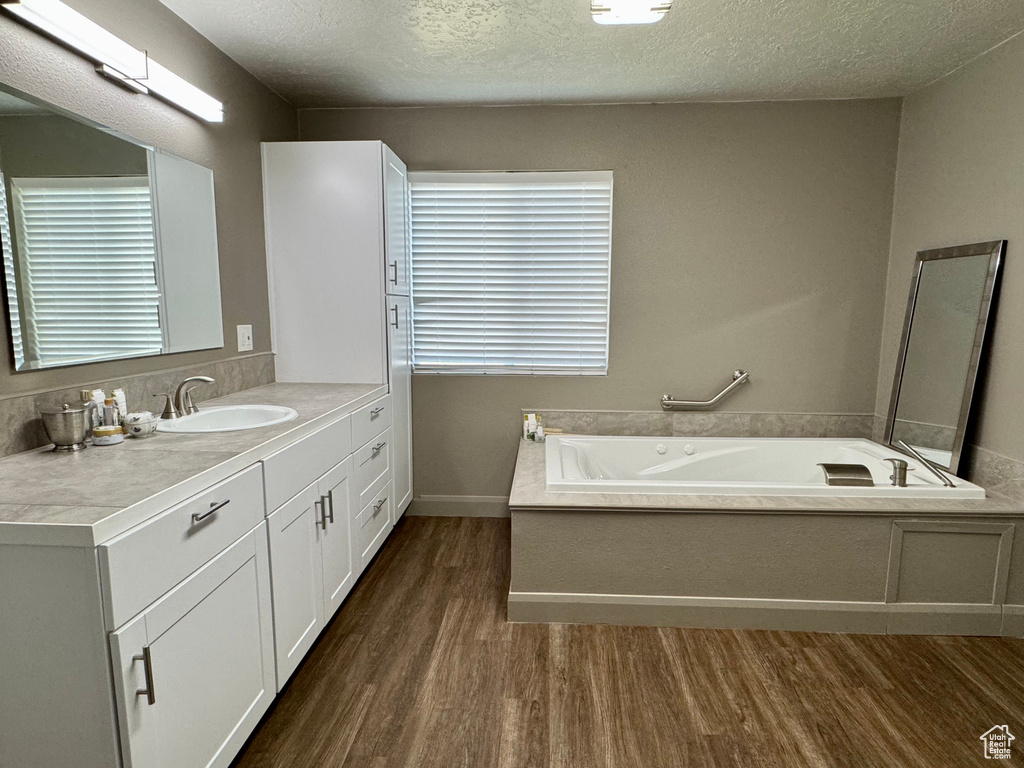 Full bath with wood finished floors, vanity, a bath, and a textured ceiling