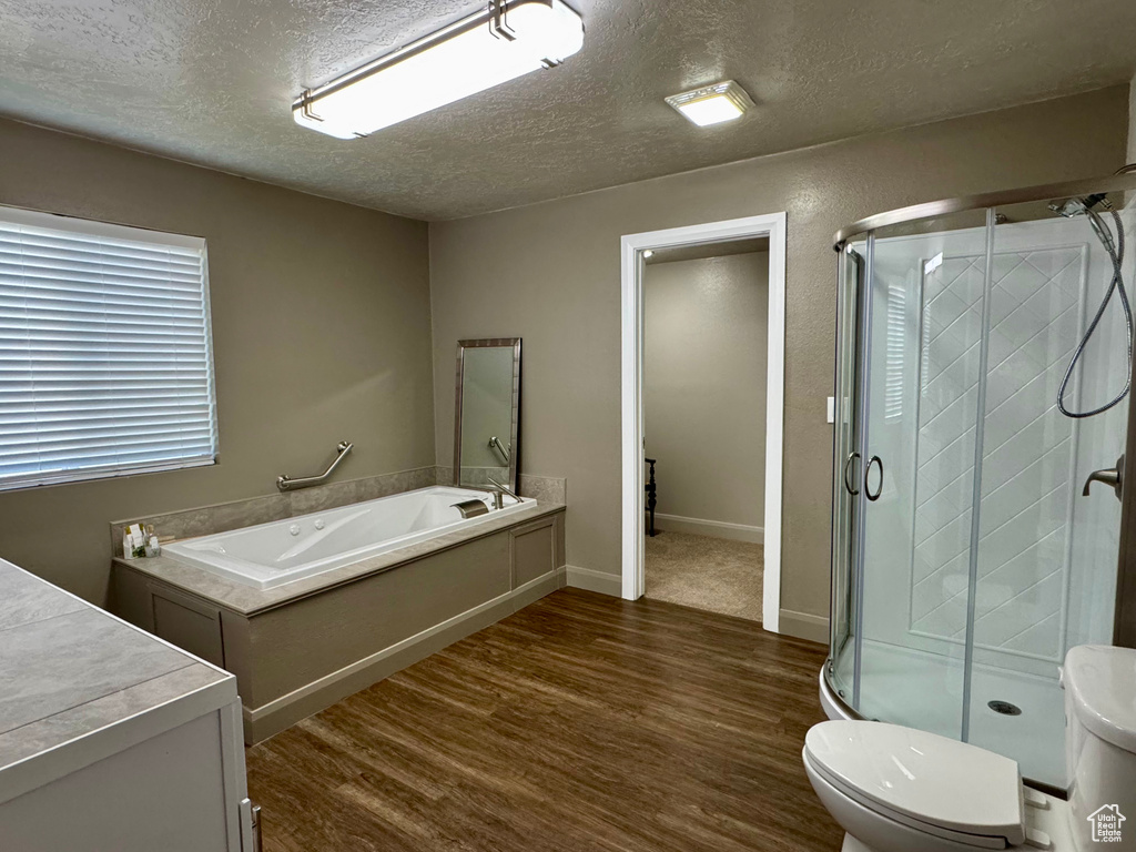 Full bath featuring wood finished floors, a textured ceiling, a stall shower, a garden tub, and toilet