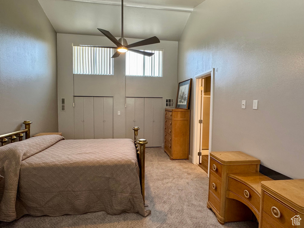 Bedroom with light colored carpet, high vaulted ceiling, multiple closets, and ceiling fan