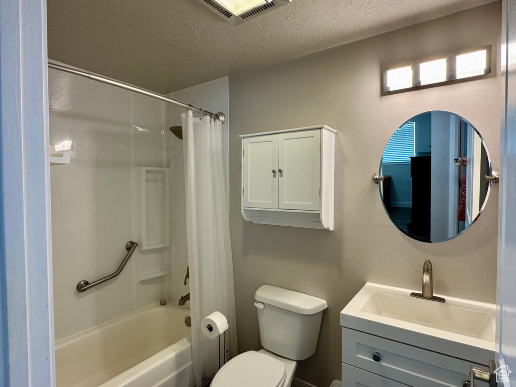 Full bathroom with a textured ceiling, vanity, toilet, and shower / bath combo